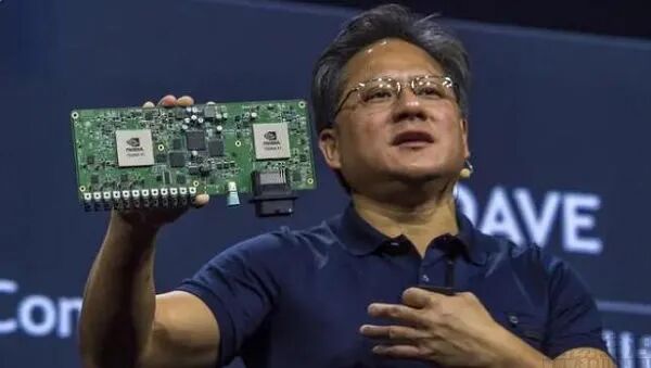 身穿深蓝色Polo衫的黄仁勋在演讲台上右手高举带有NVIDIA标志芯片的绿色电路板