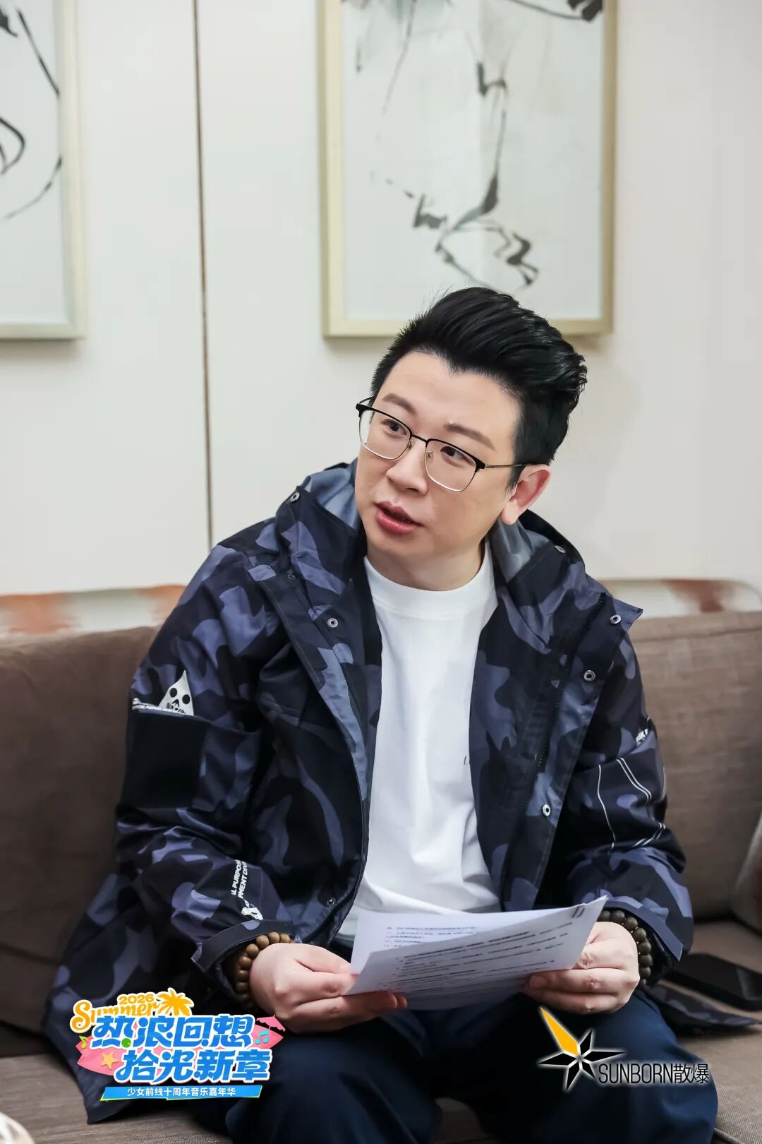 羽中坐在沙发上，手持纸质文件，背景为《少女前线》十周年嘉年华主题标识