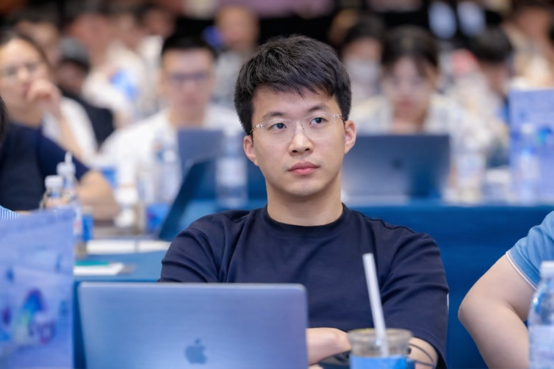 一位戴眼镜的年轻男子在讲座现场专注于前方的笔记本电脑