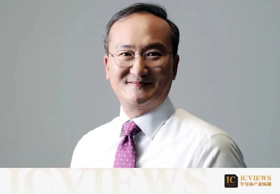 中年男性,戴圆形金属细框眼镜,身穿白色衬衫和紫色领带,面带微笑的正面照