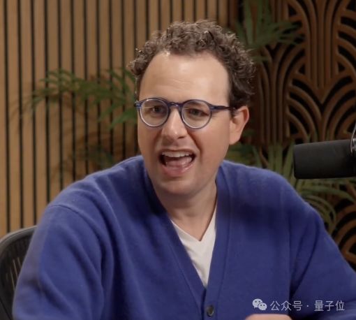 一名男士在会议中发言的照片，背景有麦克风和绿植