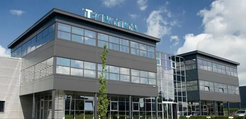 Tecnotion 公司灰色多层办公楼外观，顶部有蓝色立体字标识