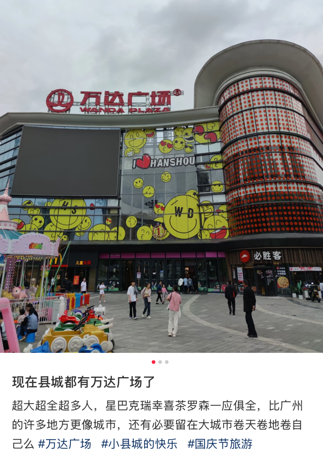 县城万达广场外景，外墙有笑脸图案和I ❤ HANSOU字样，广场前人流如织