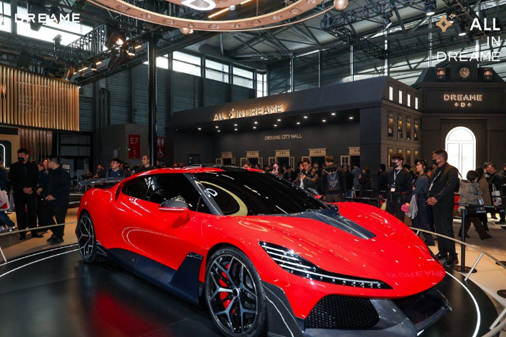 红色高性能跑车在展厅旋转展台上，配有碳纤维部件和细长LED灯带，背景有“ALL IN DREAME”和“DREAME CITY HALL”展区