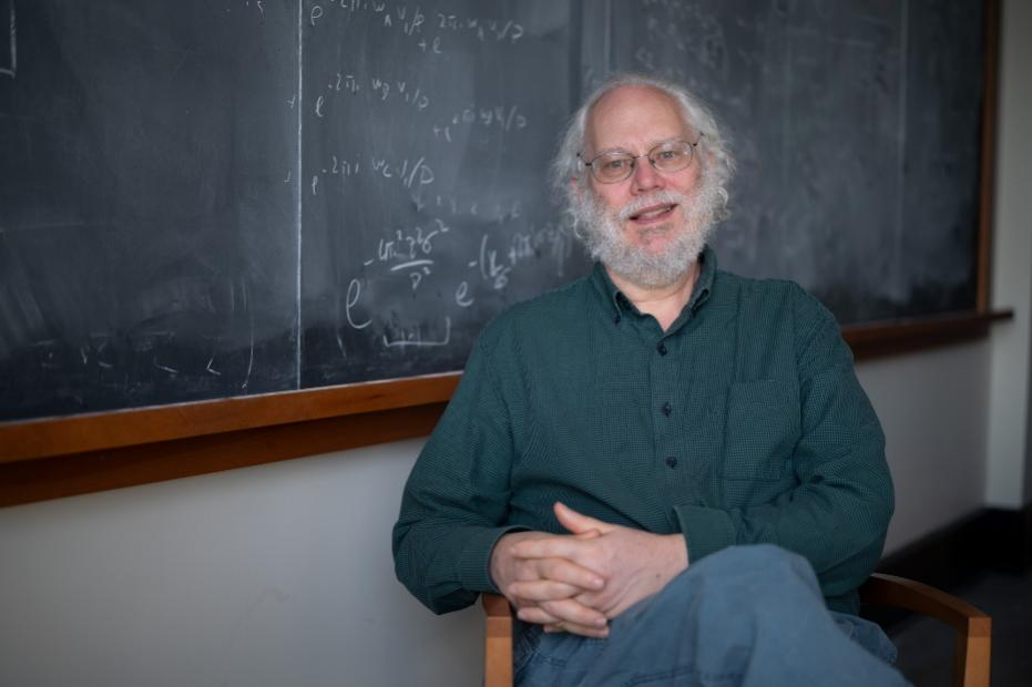 Peter Shor坐在写满公式的黑板前