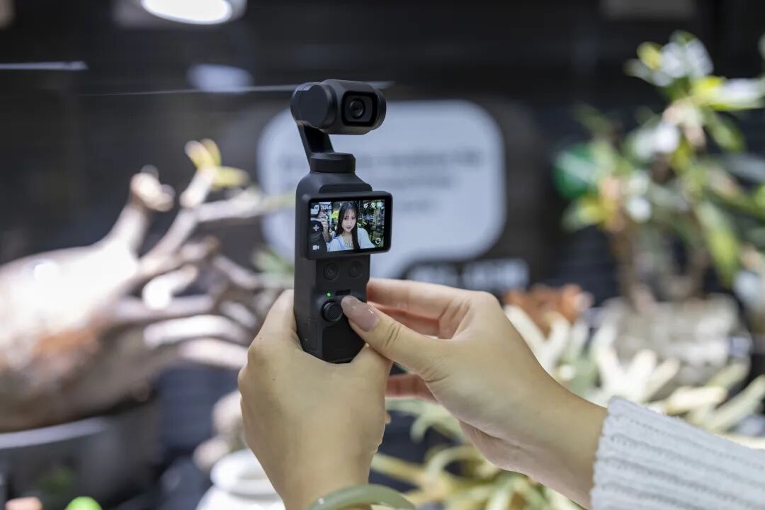 手部握持操作大疆手持云台相机，相机屏幕显示实时自拍画面