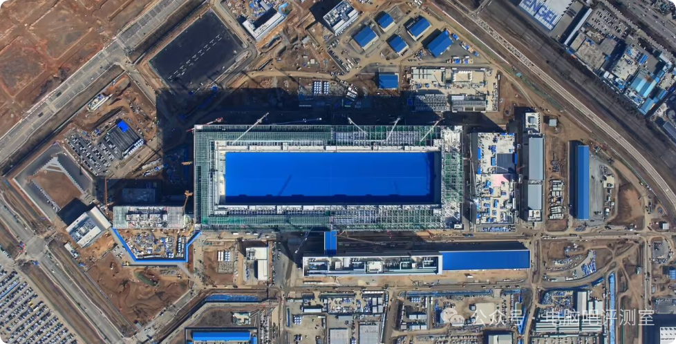 航拍视角下的大型在建半导体工厂，主体建筑覆有蓝色材料，周边布满施工设施与铁路