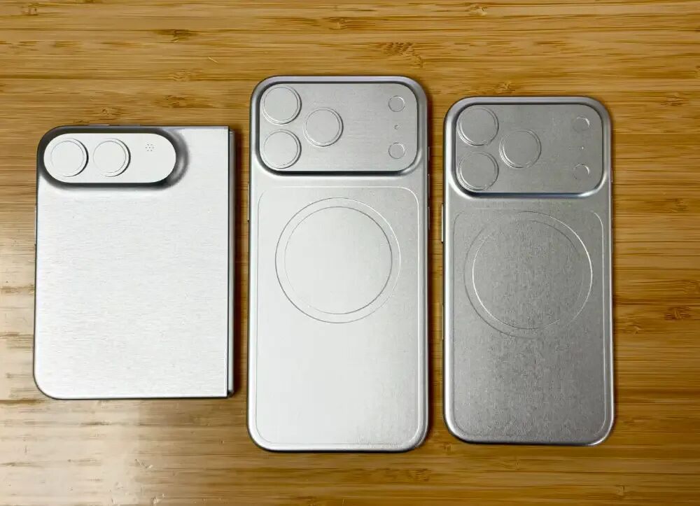 三款银色金属质感手机后盖模型并排置于竹制纹理桌面，从左至右尺寸递增，摄像头模组形态各异