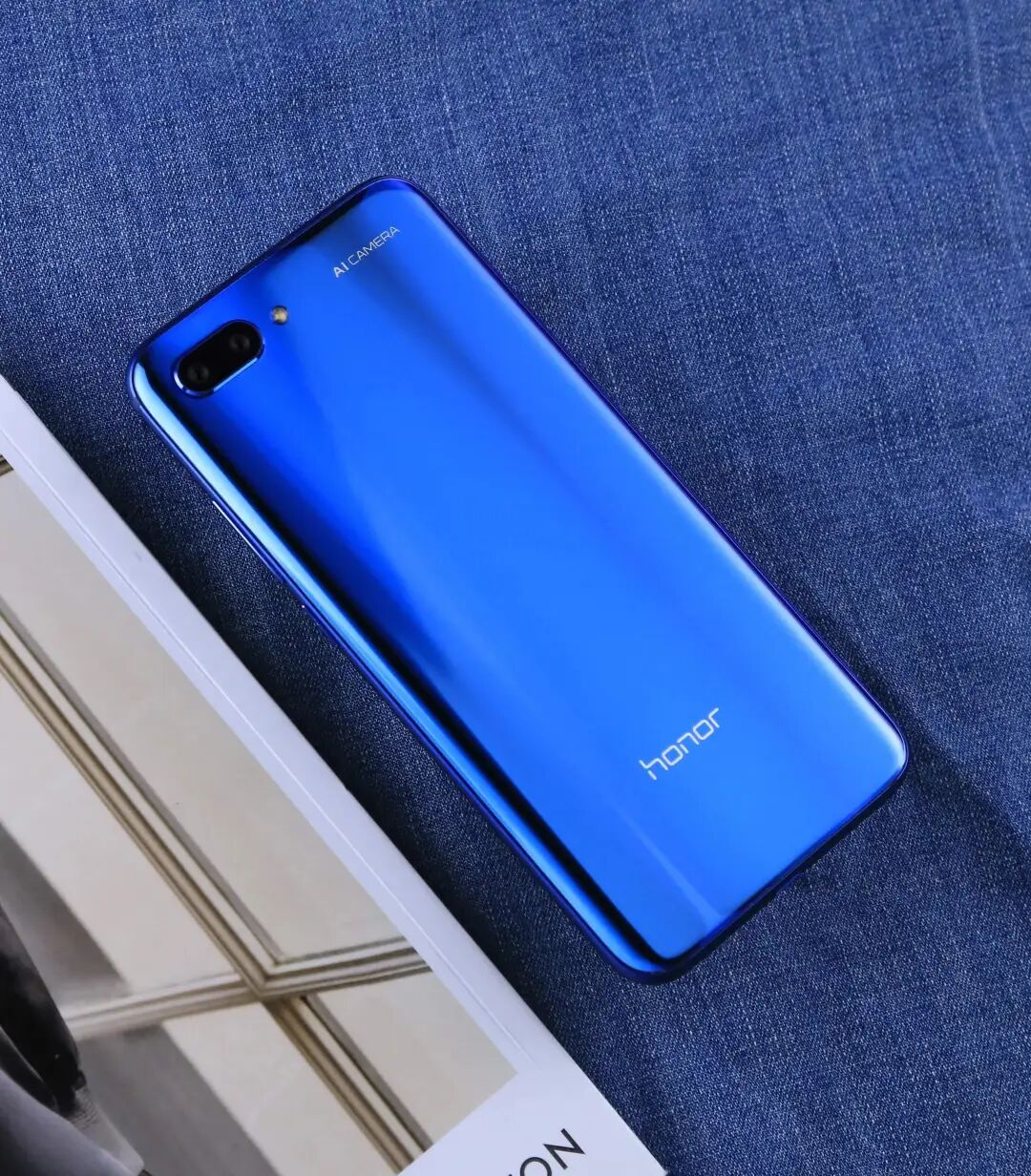 一部荣耀(honor)手机背面特写,放置在牛仔布料上,左上角有AI CAMERA标识