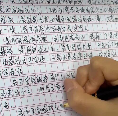 一只手握着笔正在方格纸上书写中文手写字体的特写照片