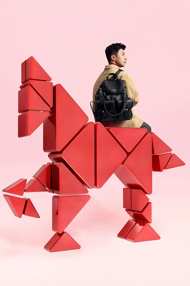 模特坐于红色几何马形雕塑上，背景纯粉，时尚广告风格