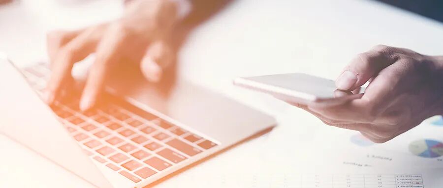 一只手在笔记本电脑上打字，另一只手拿着手机