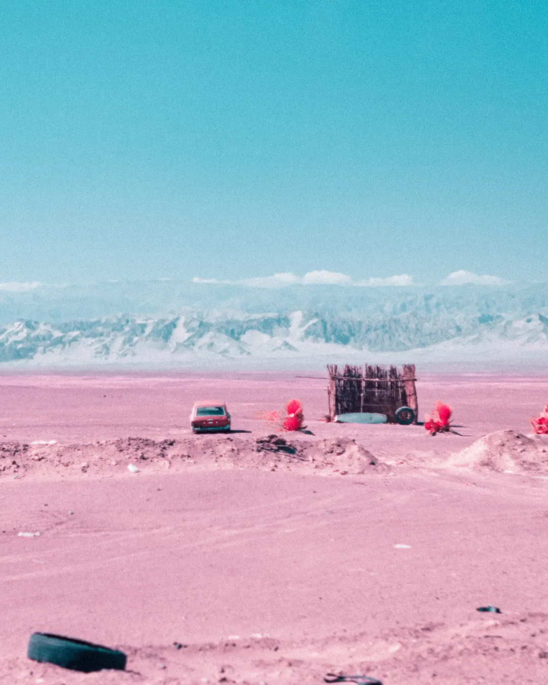 粉红色荒漠中停放的老式红色汽车与废弃轮胎