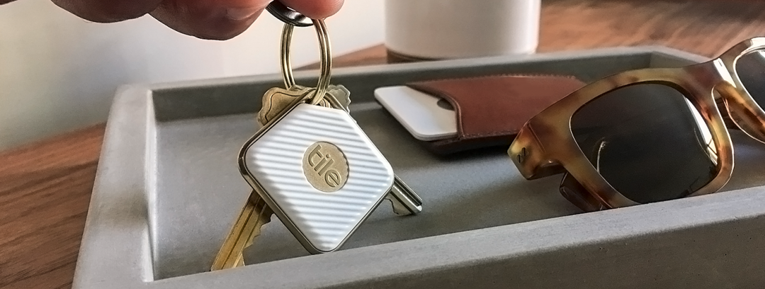 一只手拿着一串钥匙，其中一把钥匙上挂着一个白色的Tile追踪器