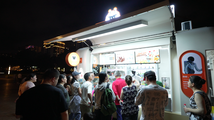 夜间移动餐车前顾客排队,车顶有发光卡通熊头招牌,车内有机器人正在操作