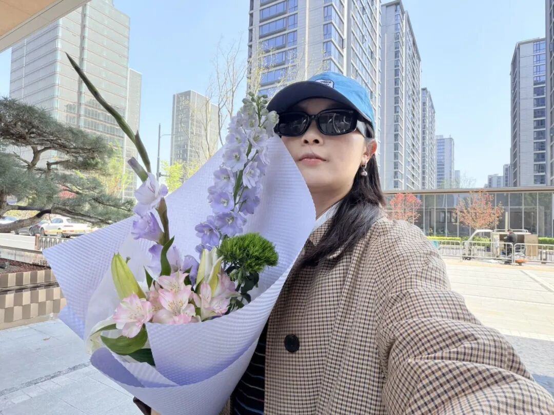 手持鲜花的女性自拍，背景为现代城市
