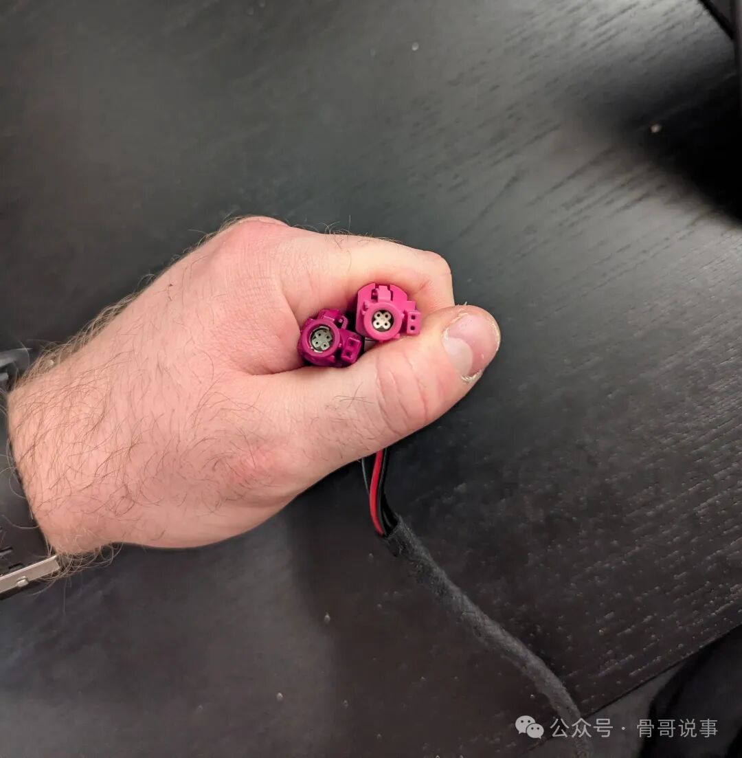 手部特写，捏着粉红色汽车线束插头，内部可见四个金属触点