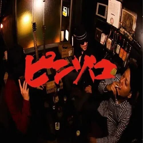 一张昏暗室内场景的照片，疑似酒吧或小型演出场所。画面中有三个人物：右侧一名穿黑白格子衬衫的男子闭眼叼着烟；中间偏后一名戴黑色帽子、穿深色衣服的人面带笑容；左侧一人穿红色上衣，手部抬起呈手势状。背景可见吉他、微波炉、老式收音机、酒瓶等物品，整体氛围复古且略显喧闹。画面中央有醒目的红色日文艺术字“ビンヤ”，字体粗犷、带有涂鸦风格，覆盖在人物和背景之上。