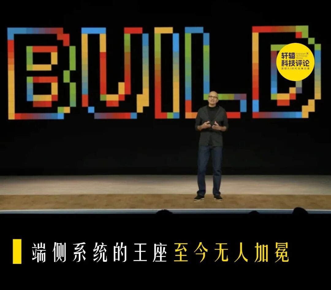 一名戴眼镜的光头男性站在舞台上，身穿深色上衣和蓝色牛仔裤，双手交叠于身前。他身后是黑色背景，上方有由彩色像素块组成的巨大英文单词“BUILD”。画面右上角有“轩辕 科技评论”水印；画面底部横幅上有文字：“端侧系统的王座至今无人加冕”。