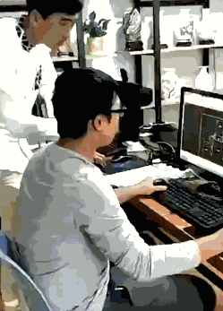 硬件工程师在电脑前修改PCB设计,同事在身后观看