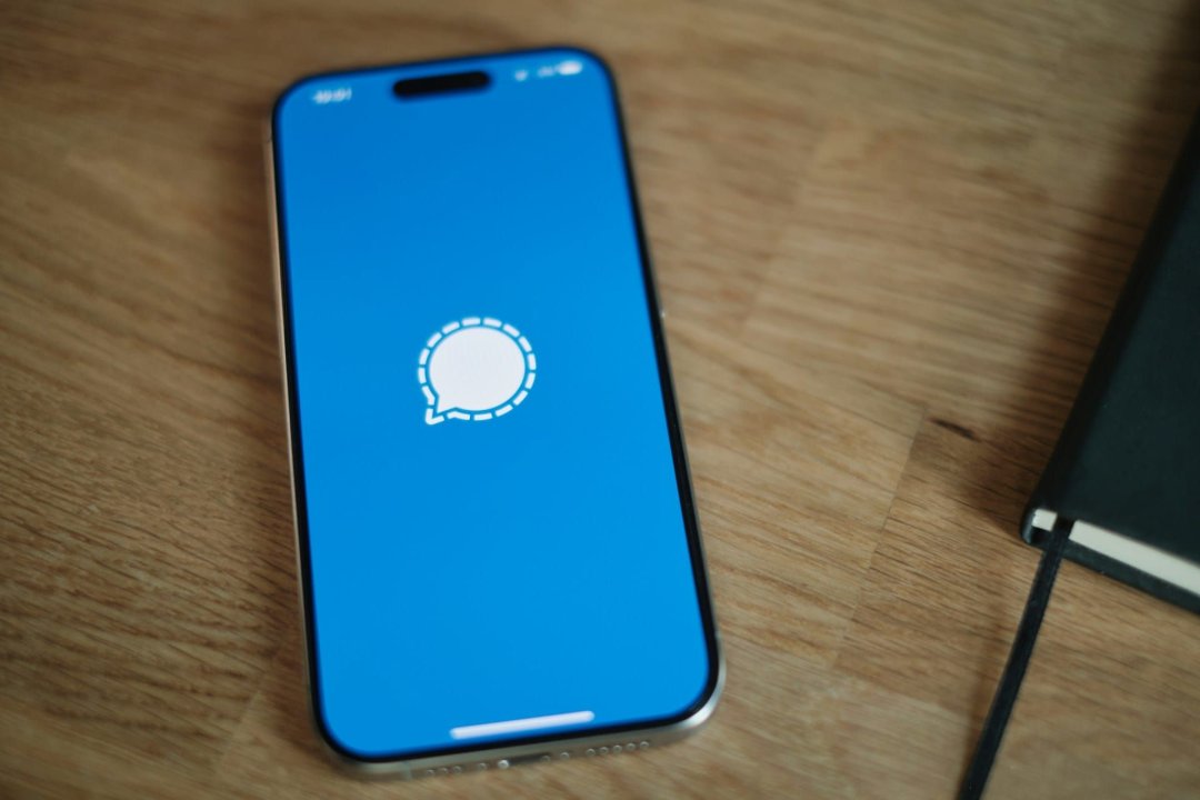 放置在木纹桌面上的金色iPhone，屏幕显示通知气泡图标