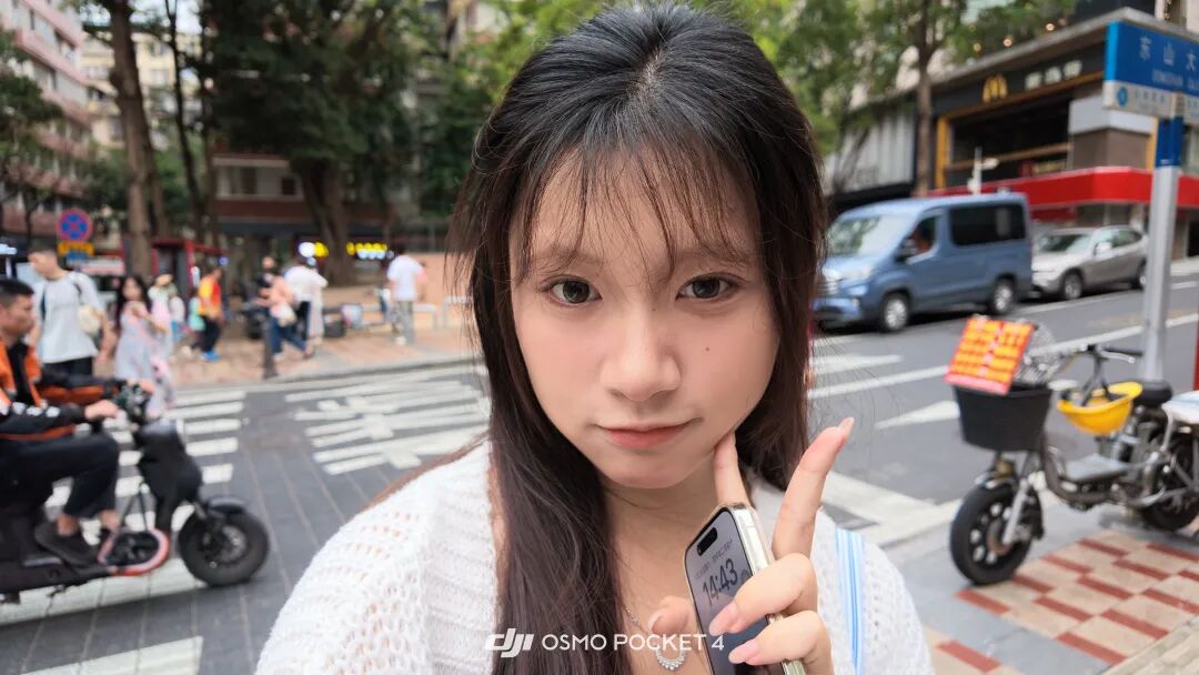 一位女性在街头用DJI OSMO POCKET 4自拍，背景为街道和行人