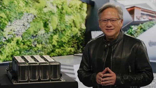 黄仁勋身穿黑色皮夹克站在一组高性能计算模块旁微笑