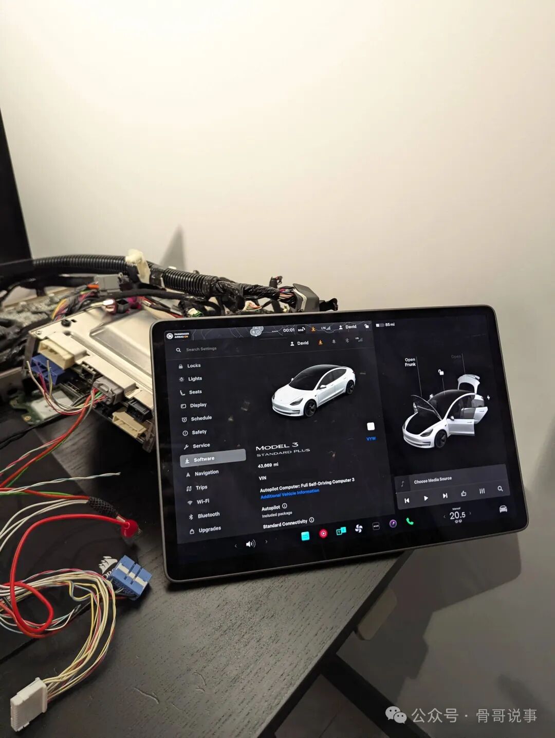 平板屏幕显示特斯拉Model 3设置界面，周围散落电子元件和线束