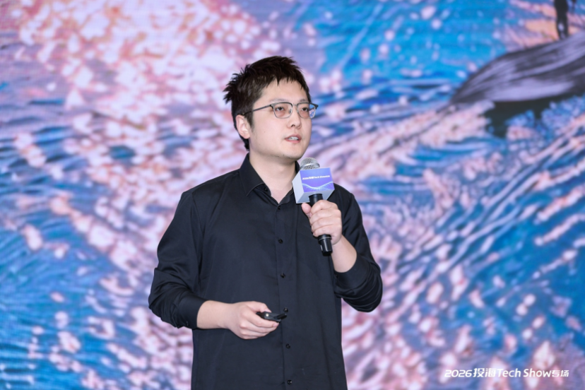 “2026投喂Tech Show专场”一名戴眼镜的短发男性手持麦克风在舞台上演讲