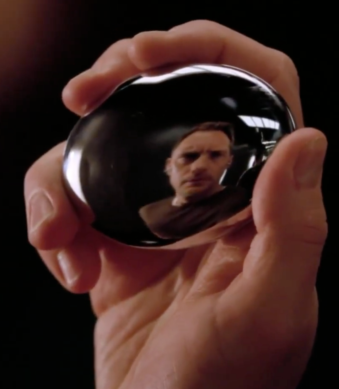 一只手持握着一枚光滑的黑色椭球体,表面倒映出人脸