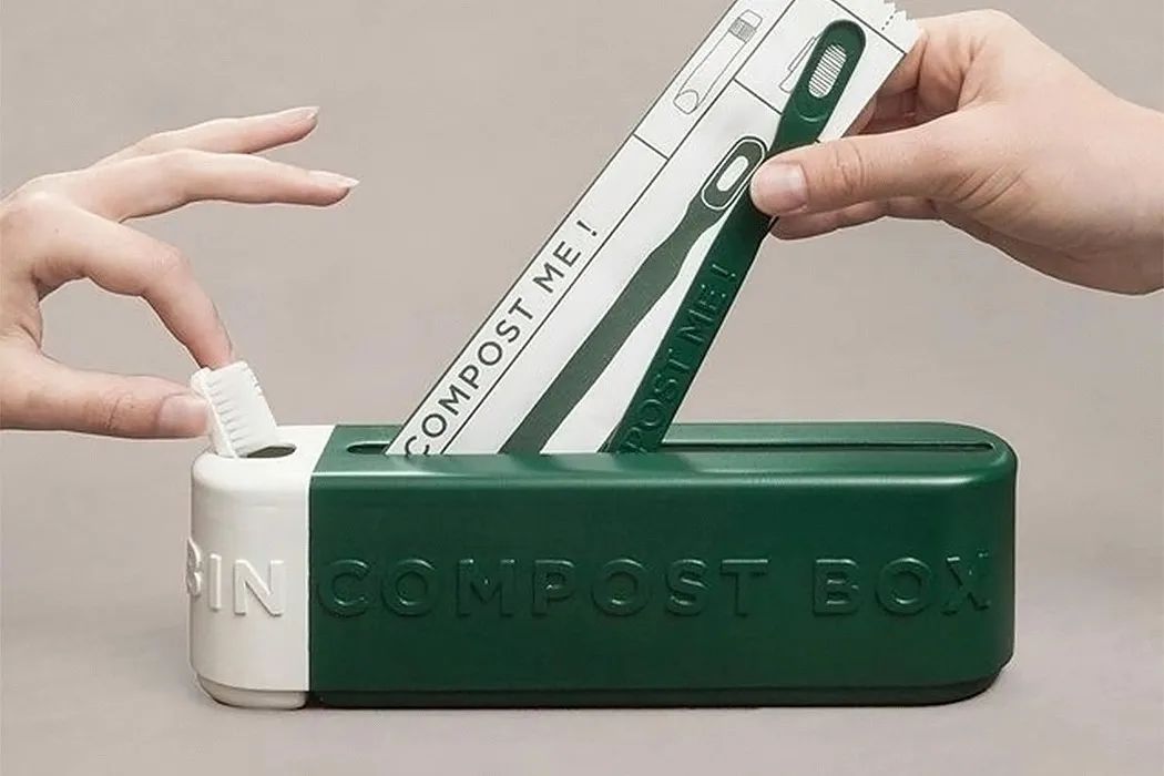 手将牙刷包装盒插入绿色 compost box 中