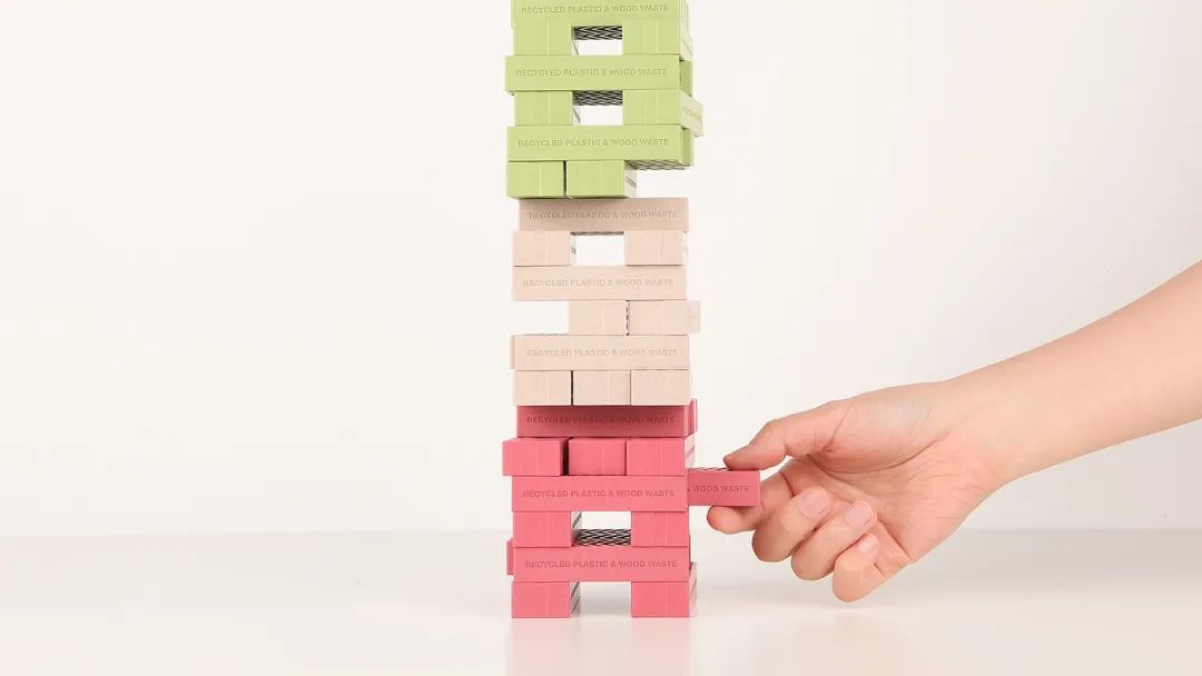 手从积木塔中抽出一块印有再生材料字样的积木