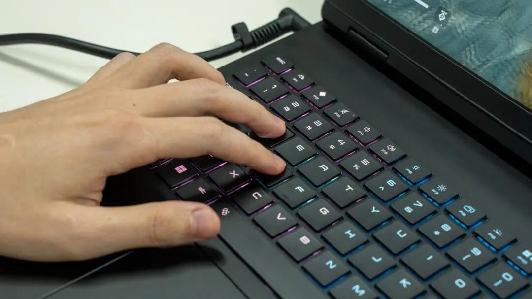 一只手正在操作带有紫色蓝色渐变背光的笔记本电脑键盘