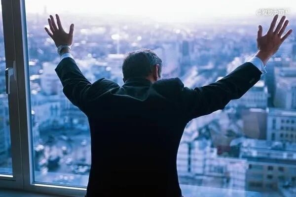 一名男子背对城市站在落地窗前