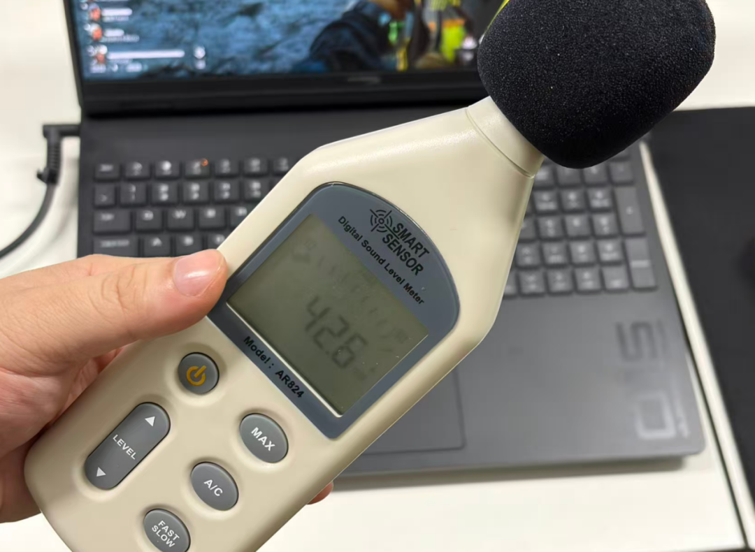 手持数字声级计贴近笔记本电脑测量噪音，屏幕显示当前读数为42.6dB