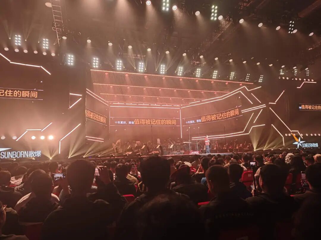 十周年音乐嘉年华现场，聚光灯与舞台屏幕映出“值得被记住的瞬间”