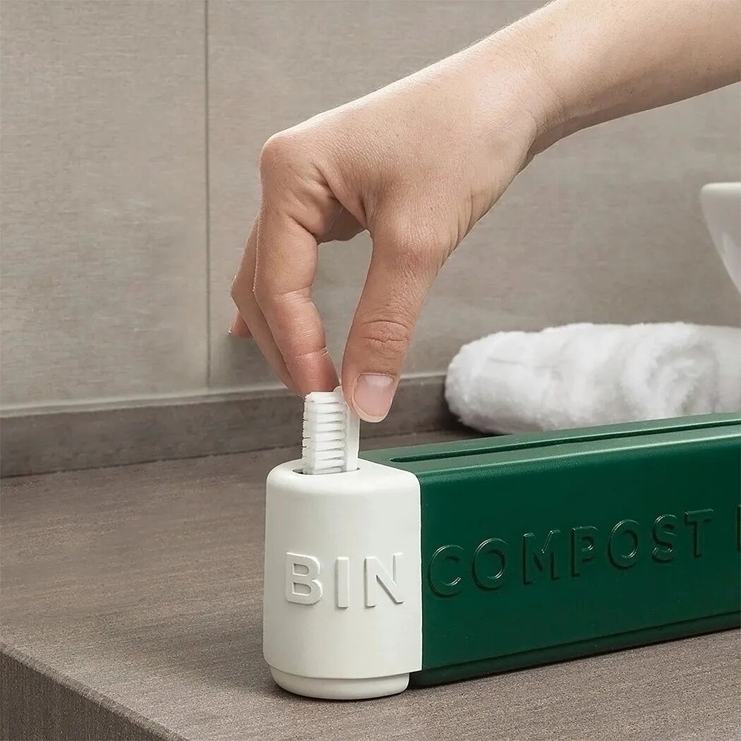 手将牙刷插入白色装置，旁边是绿色堆肥桶