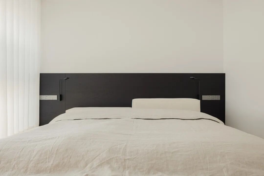 现代简约卧室床铺特写，黑色床头板与壁灯
