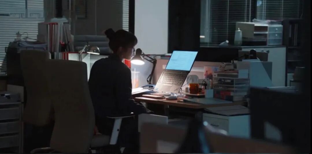 昏暗办公室中，一名女性背对镜头用电脑工作