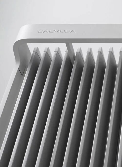 刻有BALMUDA品牌字样的流线型设备顶部，下方为密集平行竖直散热片结构