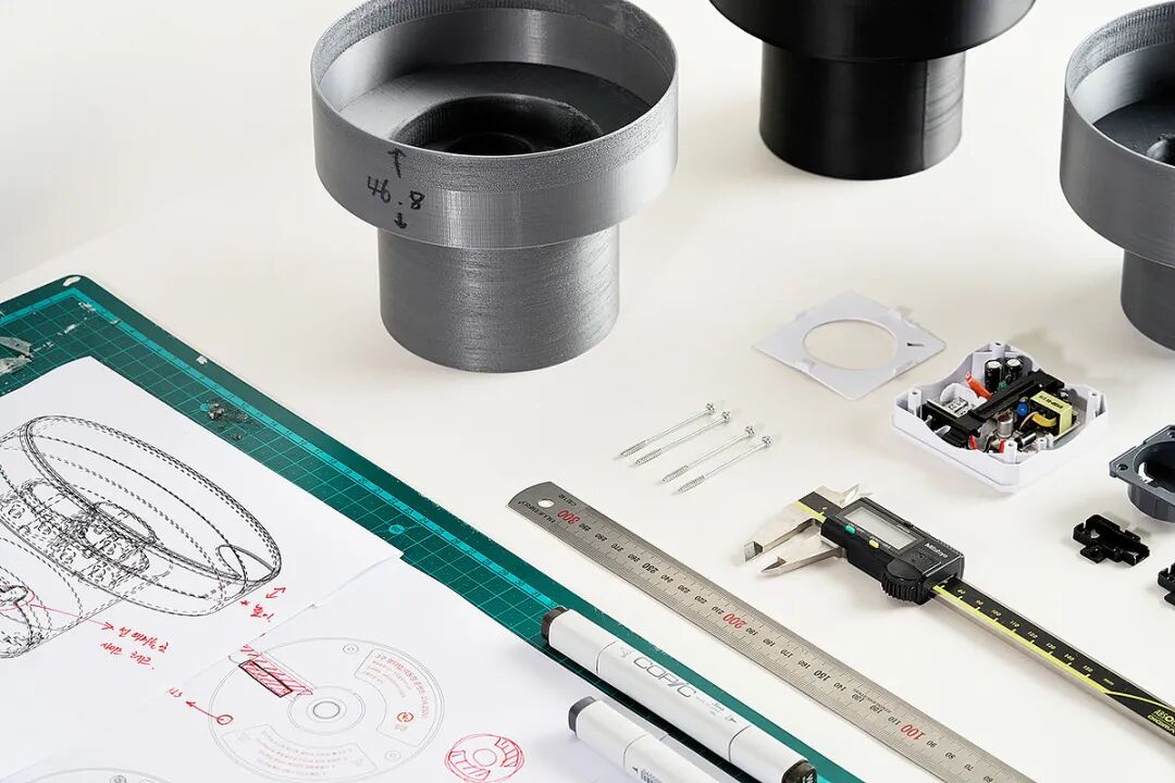 一张展示3D打印零件、电子元件和设计图纸的桌面场景