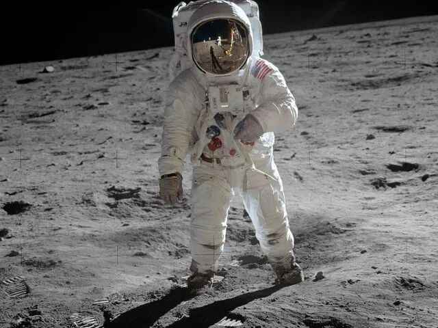 宇航员站在月球表面,头盔面罩反射出登月舱轮廓
