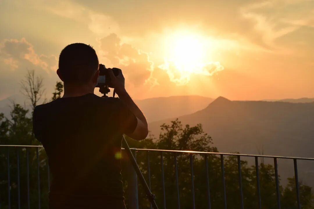 摄影师在夕阳余晖中架着三脚架拍摄山峦落日剪影