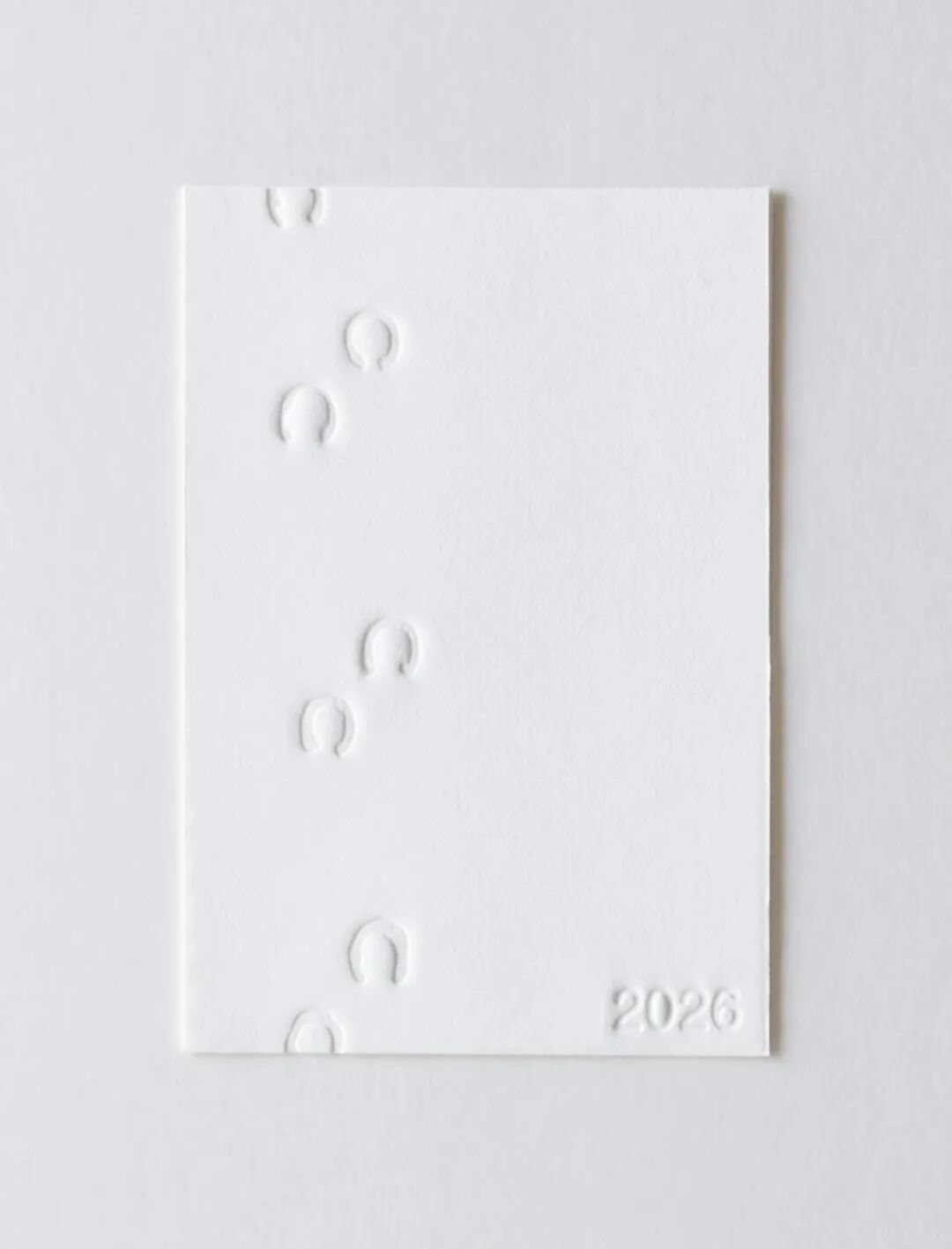 白色贺卡上几枚凸起的马蹄印，右下角印有“2026”，极简主义风格