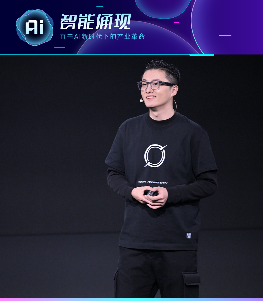 一位戴黑框眼镜、耳挂麦克风的中年男性站在深色舞台上，身后是“智能涌现”主题的科技风格背景板