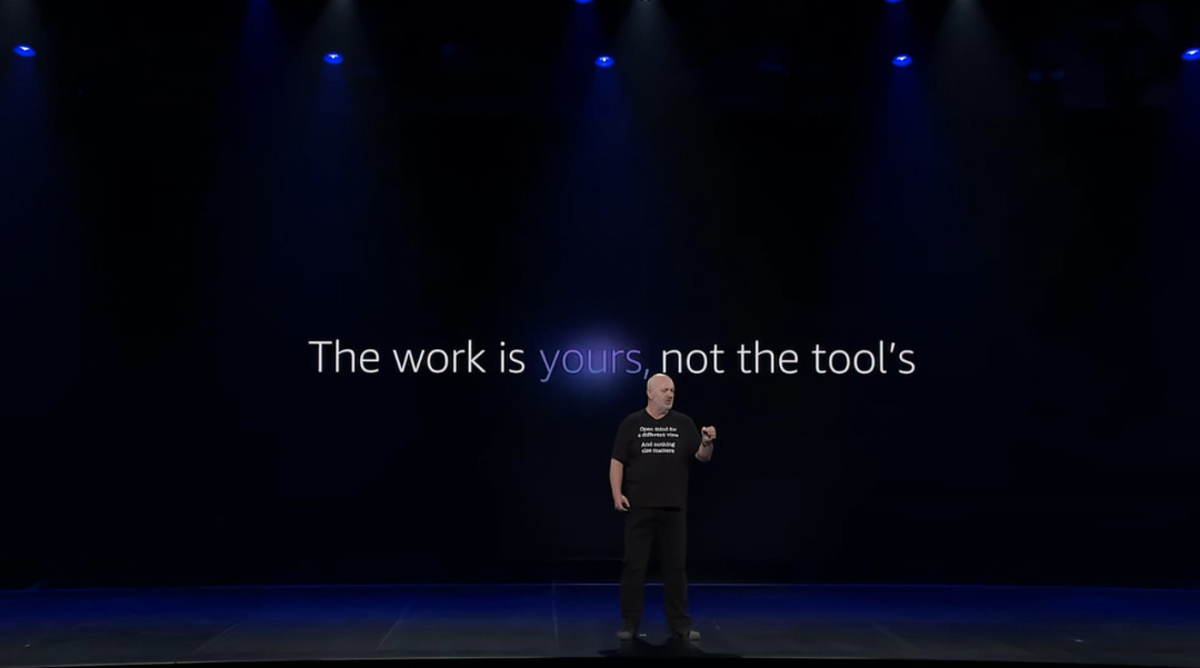 Werner Vogels在re:Invent舞台上演讲,背景标语写着"The work is yours, not the tool's"
