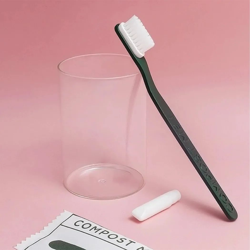 粉色背景下斜靠在玻璃杯旁的深绿色牙刷