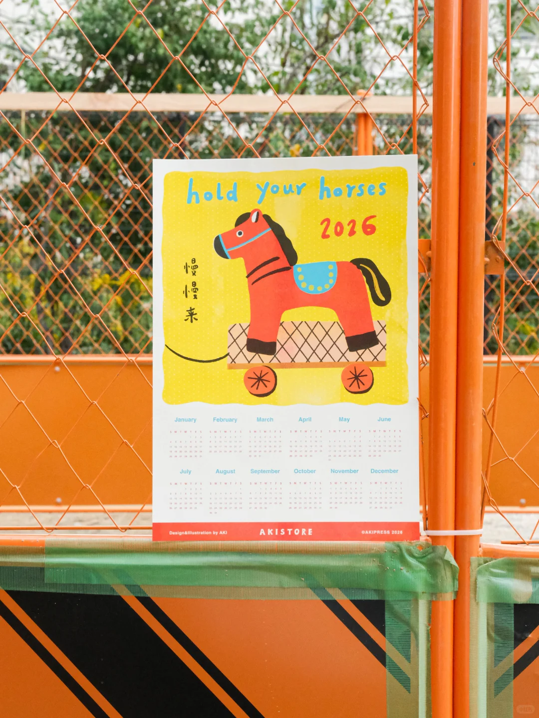 红色背景日历海报：黄色木马，蓝色马鞍，“hold your horses 2026”，左侧“慢慢来”