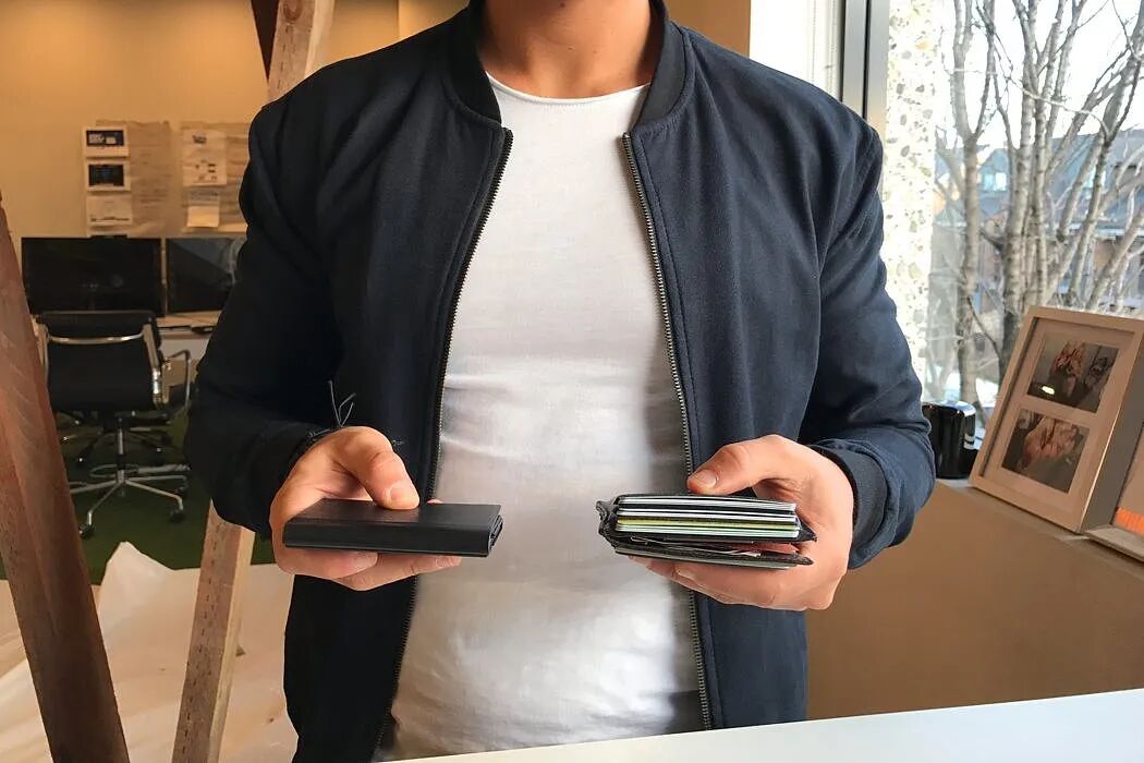 一名穿着深色夹克和白色T恤的男子站在室内，双手各持一个物品