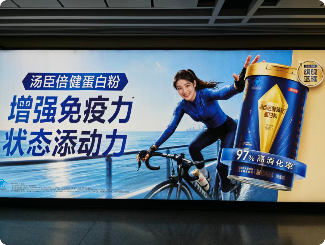 汤臣倍健蛋白粉地铁户外广告牌,展示AI生成的蓝罐产品和骑行女性形象
